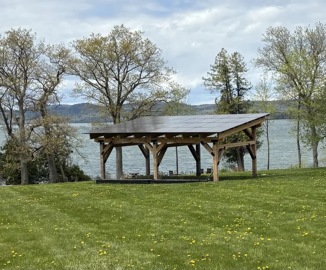 Completed timber-frame Sunport with a solar roof on a lawn above Lake Champlain