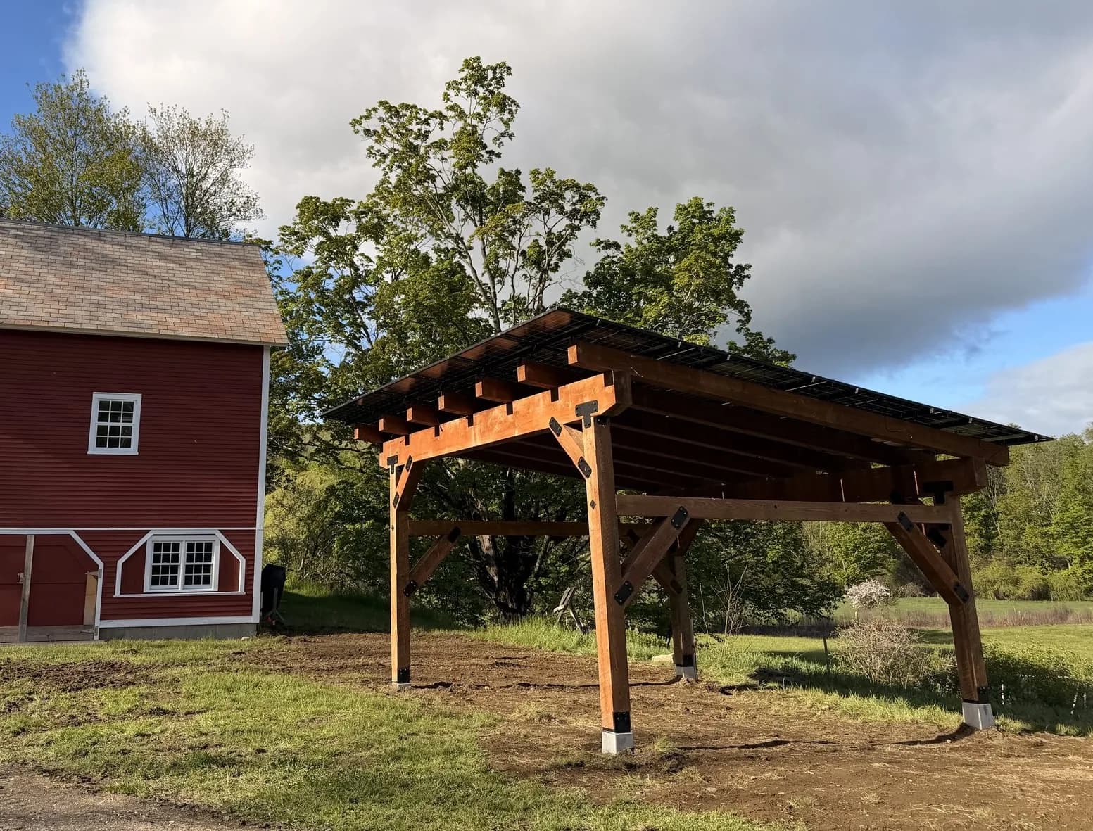 Timber-frame Sunport beside a red barn on a Vermont property